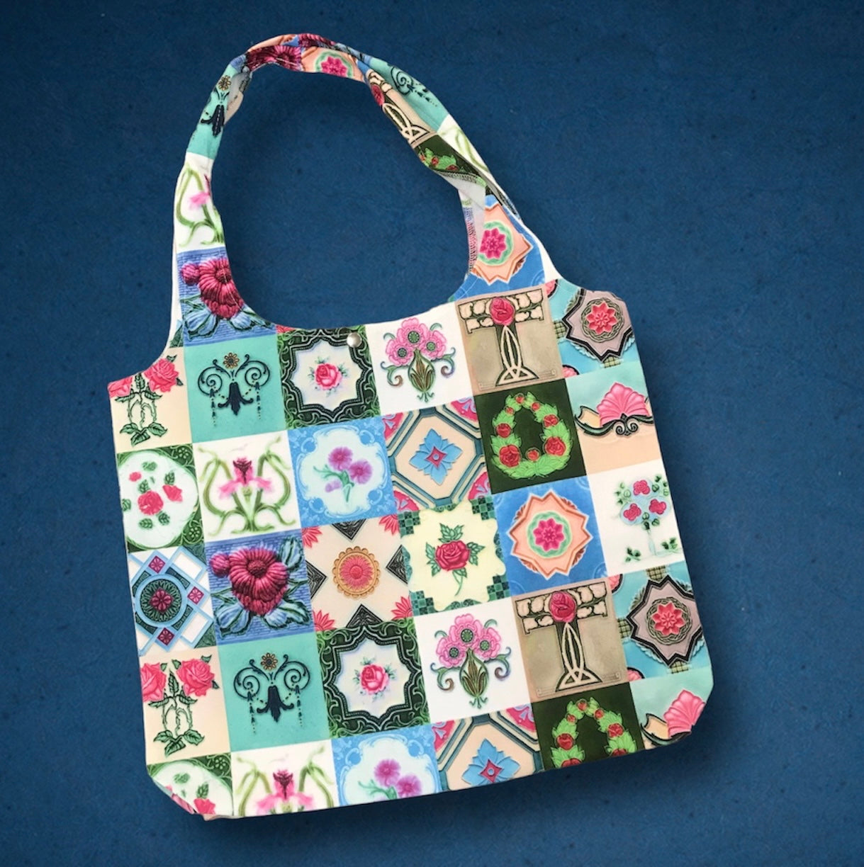 A foldable tote bag with a multicolored floral pattern, featuring Peranakan tiles.