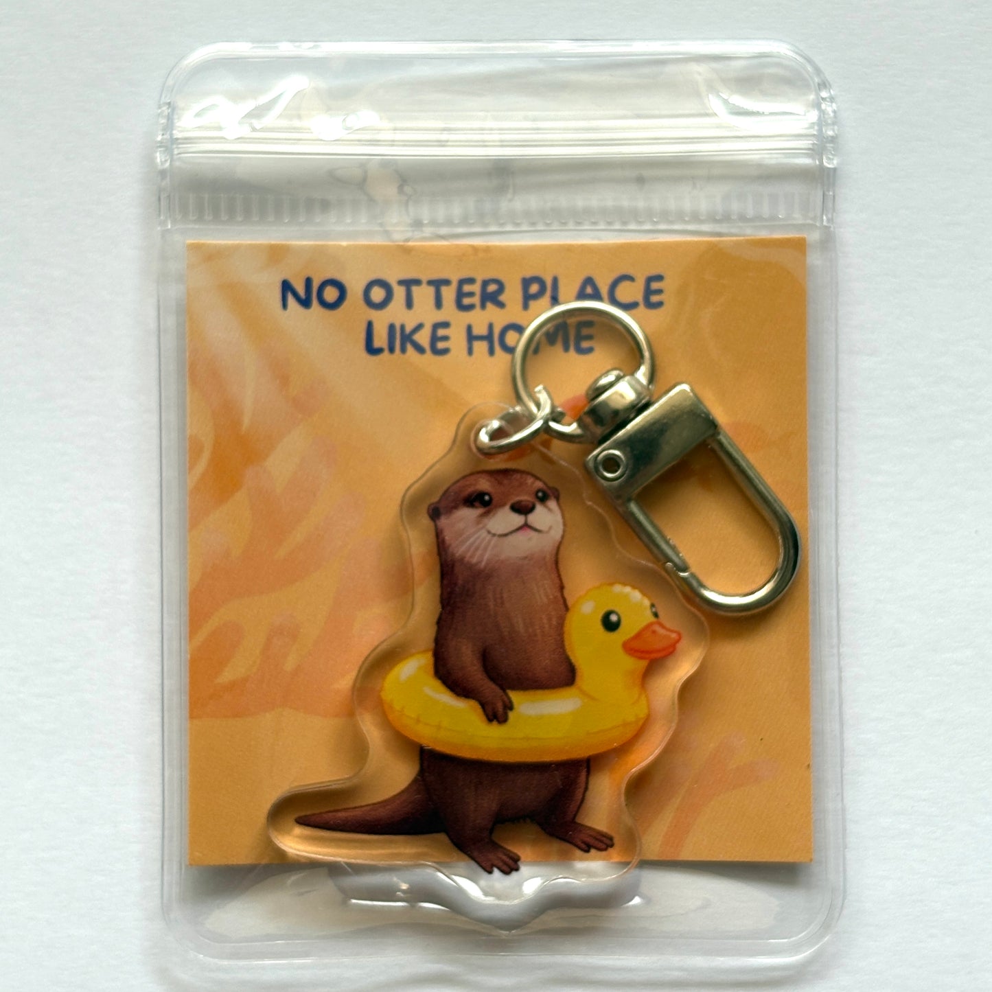 Keychain with otter and a duck float design on a card with 'No Otter Place Like Home' text.