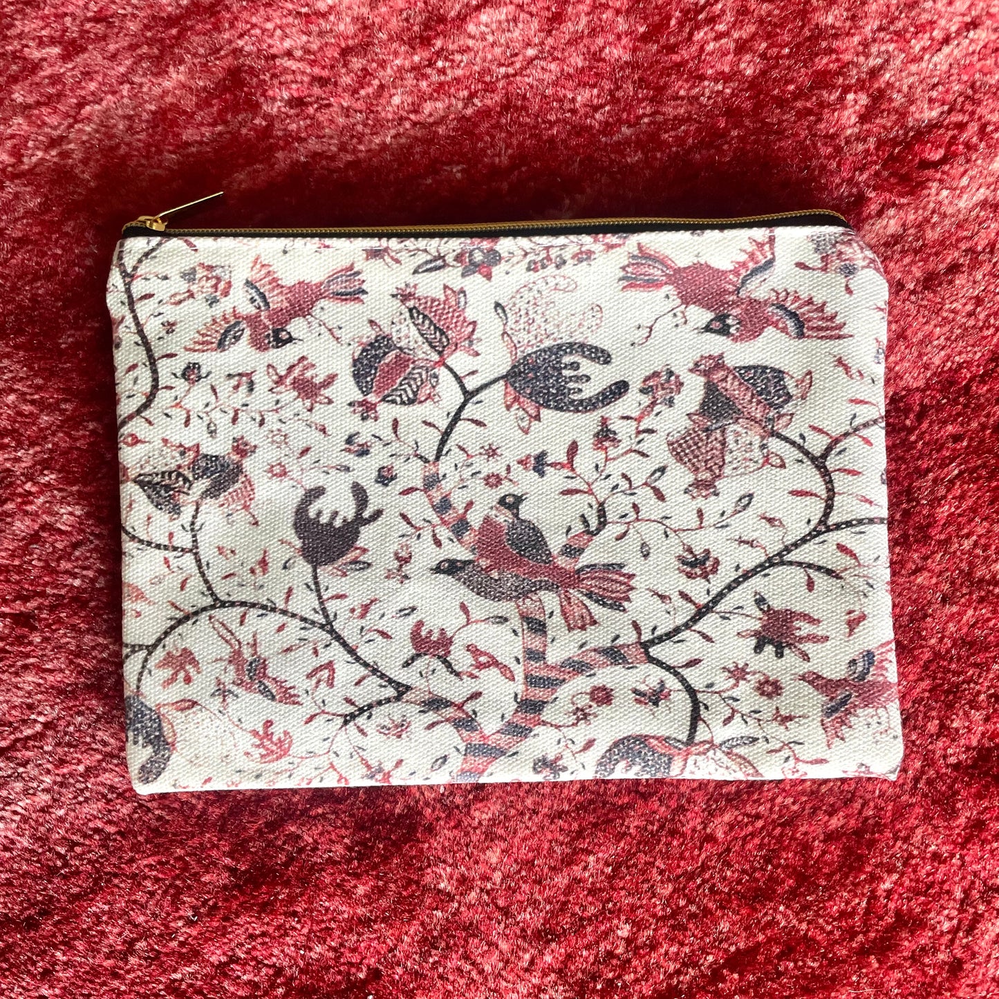 Straits Batik Pouch. A rectangular pouch with a gold zip closure, featuring a white background with red and black Javanese batik patterns, including birds and geometric motifs.