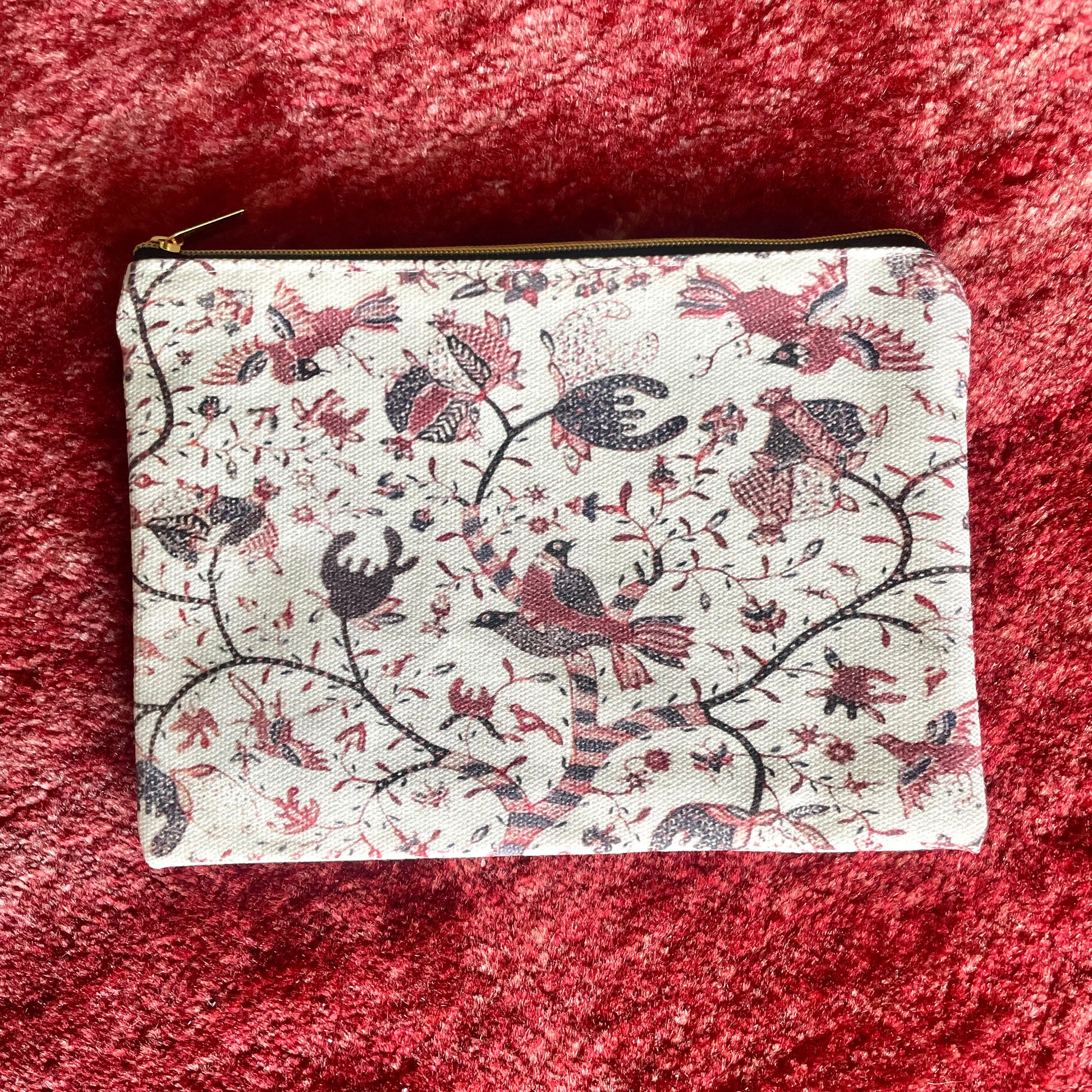 Straits Batik Pouch. A rectangular pouch with a gold zip closure, featuring a white background with red and black Javanese batik patterns, including birds and geometric motifs.